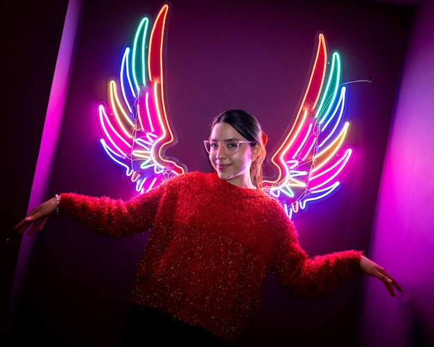 jeune fille latine souriante, avec des ailes de néon en couleur.