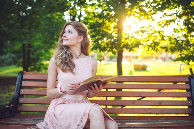 Une jeune fille lisant un livre assis sur un banc au coucher du soleil.