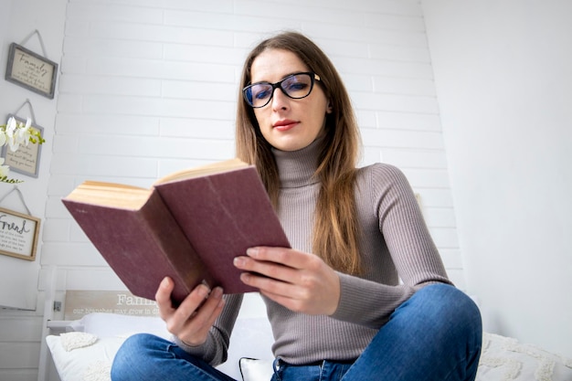 Jeune fille lisant un livre en tailleur assis sur le lit dans la chambre