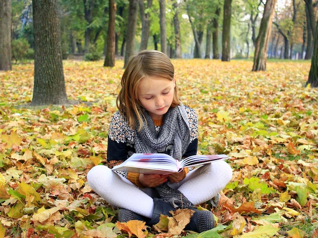 une jeune fille lit un livre dans le parc d'automne allongée sur le sol