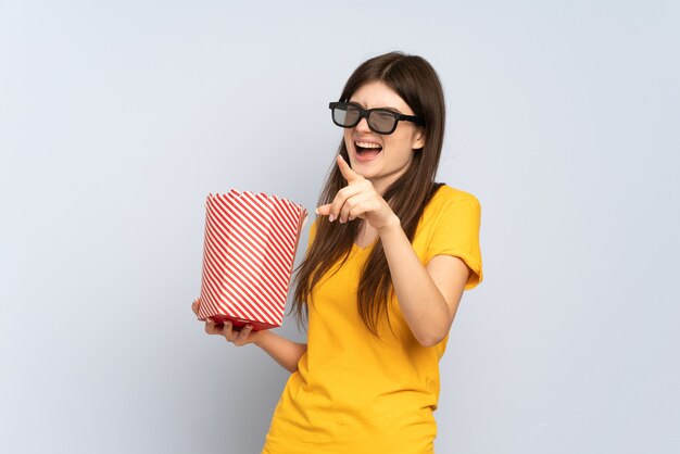 Jeune fille avec des lunettes 3D et tenant un grand seau de pop-corn tout en pointant vers l'extérieur