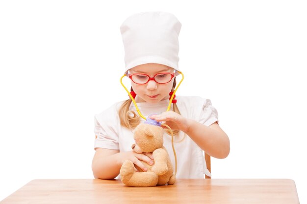 Une jeune fille à lunettes joue chez le médecin en tant que maman et traite des jouets