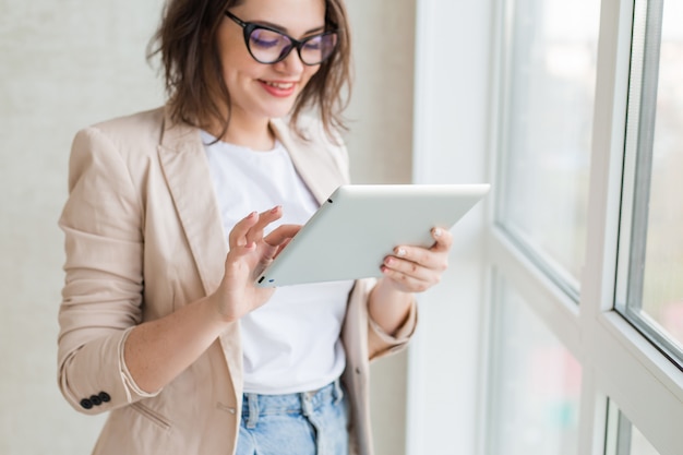 Jeune Fille à Lunettes Pour La Vision Se Tient à Côté De La Fenêtre De La Maison Tenant Une Tablette