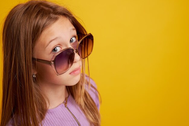 Une jeune fille à lunettes les regarde sous son front sur un fond jaune propre