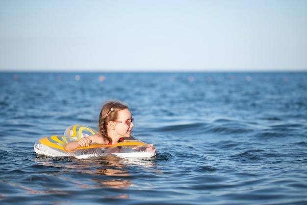 Jeune fille à lunettes rouges et un maillot de bain vert reposant sur la mer. enfance et air marin
