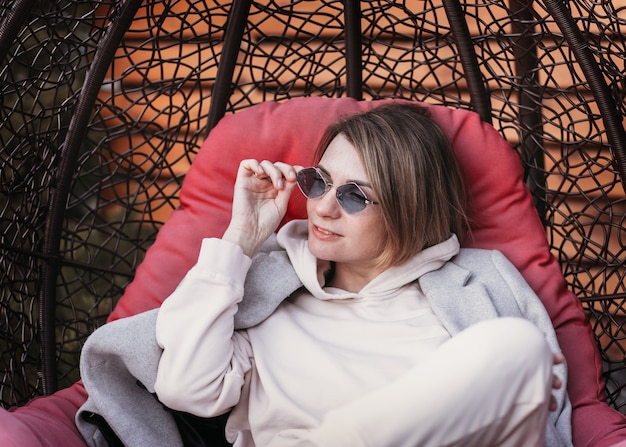 Une jeune fille à lunettes de soleil repose dans la nature sur une chaise