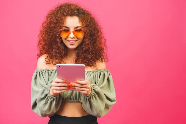 Une jeune fille à lunettes de soleil et tenant une tablette et souriant