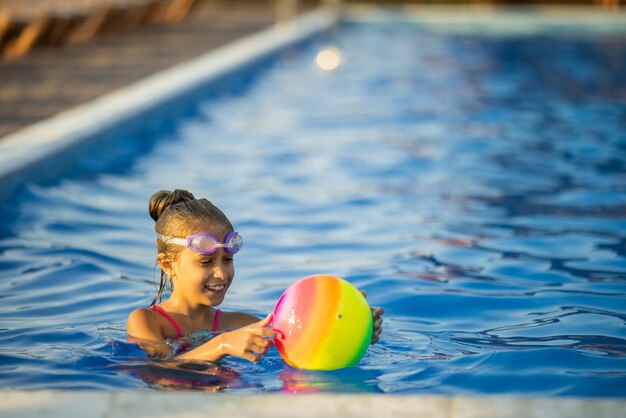 Photo une jeune fille en maillot de bain léopard brillant nage avec un ballon gonflable de couleur vive dans une piscine d'un bleu profond avec de l'eau claire et transparente lors d'une chaude soirée d'été ensoleillée