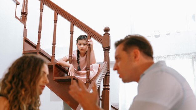 Une jeune fille malheureuse regarde ses parents se disputer depuis l'escalier Synchronos