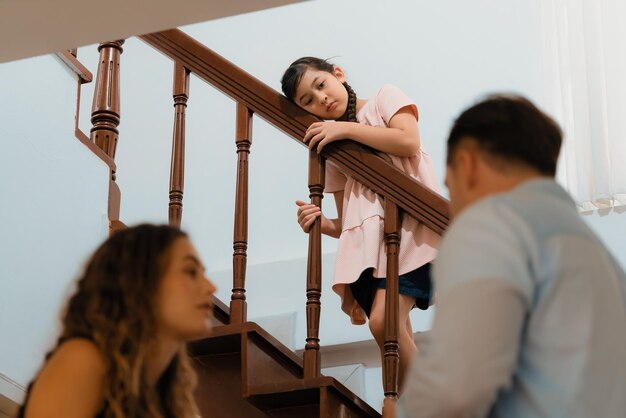 Une jeune fille malheureuse regarde ses parents se disputer depuis les escaliers.