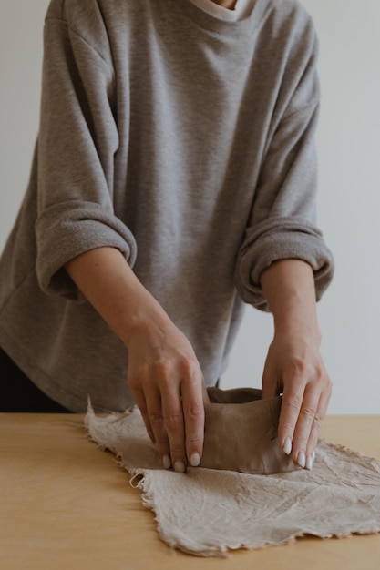 Une jeune fille en manche longue grise fabrique de ses propres mains un vase d'argile dans un atelier de sculpture