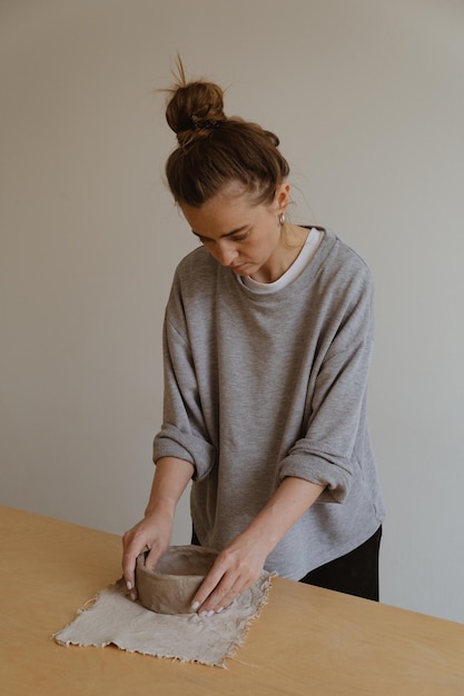 Une jeune fille en manche longue grise fabrique de ses propres mains un vase d'argile dans un atelier de sculpture