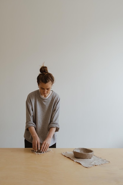 Une jeune fille en manche longue grise fabrique de ses propres mains un vase d'argile dans un atelier de sculpture