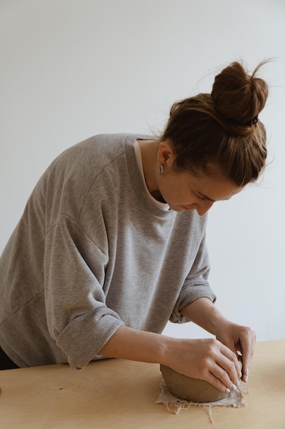 Une jeune fille en manche longue grise fabrique de ses propres mains un vase d'argile dans un atelier de sculpture