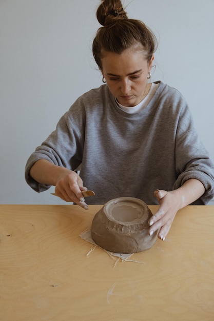 Une jeune fille en manche longue grise fabrique de ses propres mains un vase d'argile dans un atelier de sculpture