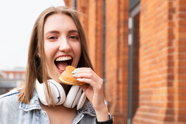 Une jeune fille mange son hamburger dans la rue. Elle s'amuse en dégustant une délicieuse collation.