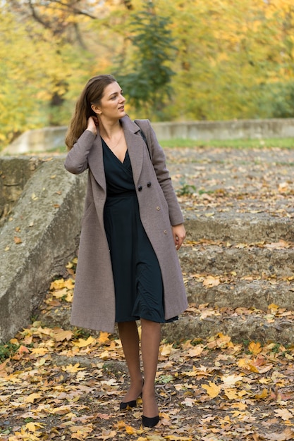 Une jeune fille en manteau pose dans un parc sur fond de feuillage d'automne doré.