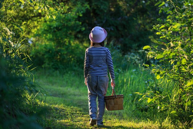 Jeune fille marchant sur un chemin à travers les bois verts portant un panier en écorce de bouleau