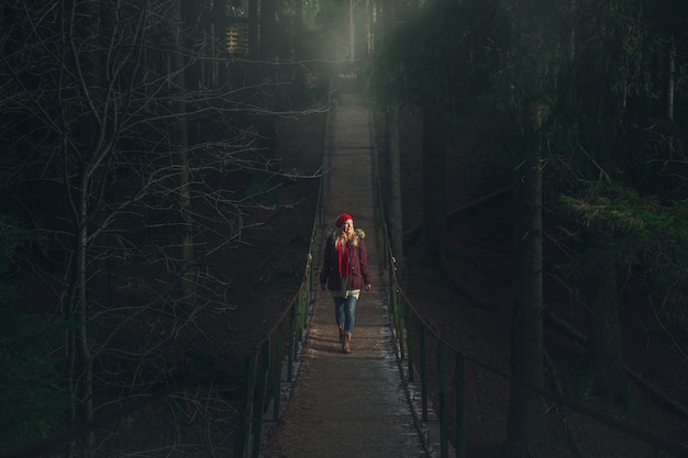 La jeune fille marche sur un pont suspendu au-dessus d'une rivière de montagne. Forêt sombre et mystique.