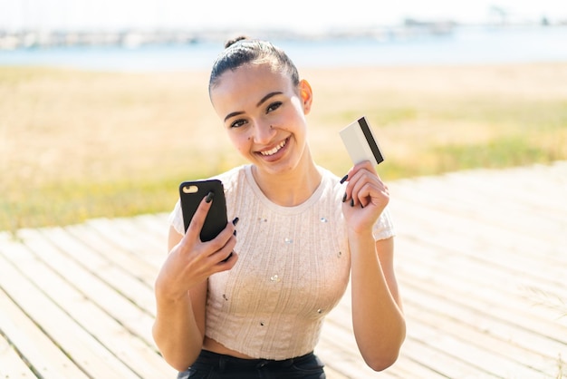 Jeune fille marocaine à l'extérieur achetant avec le mobile avec une carte de crédit