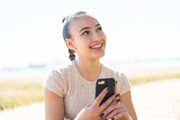 Jeune fille marocaine à l'extérieur à l'aide d'un téléphone portable et levant les yeux