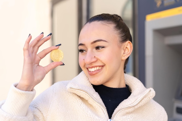 Jeune fille marocaine à l'extérieur tenant un Bitcoin et le regardant