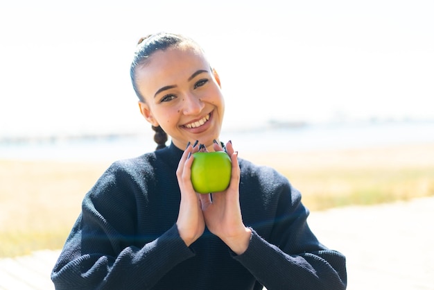 Jeune fille marocaine à l'extérieur tenant une pomme avec une expression heureuse