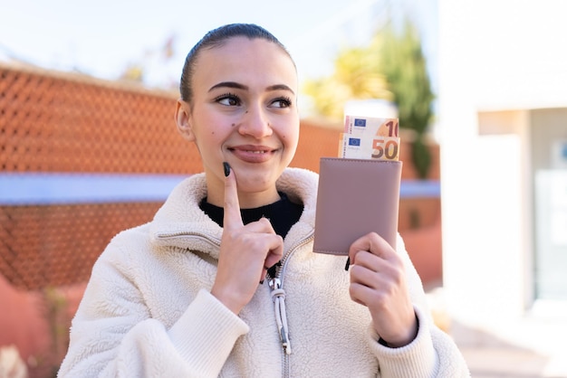 Jeune fille marocaine à l'extérieur tenant un portefeuille avec de l'argent