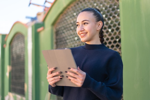 Jeune fille marocaine à l'extérieur tenant une tablette avec une expression heureuse