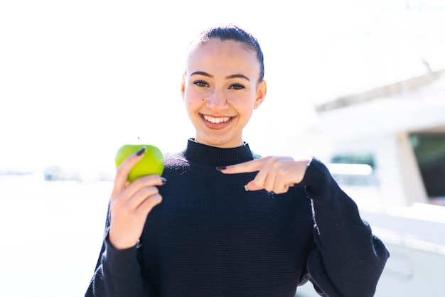 Jeune fille marocaine avec une pomme à l'extérieur et la pointant