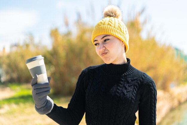 Jeune fille marocaine portant des manchons d'hiver tout en tenant un café à l'extérieur avec une expression triste