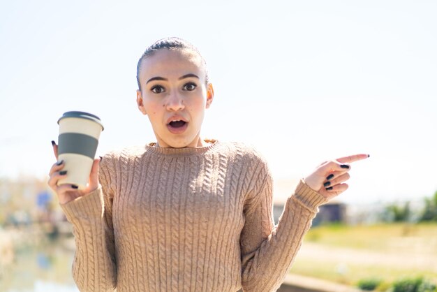 Jeune fille marocaine tenant un café à emporter à l'extérieur surpris et pointant du côté