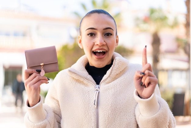 Photo jeune fille marocaine tenant un portefeuille à l'extérieur pointant vers le haut une bonne idée