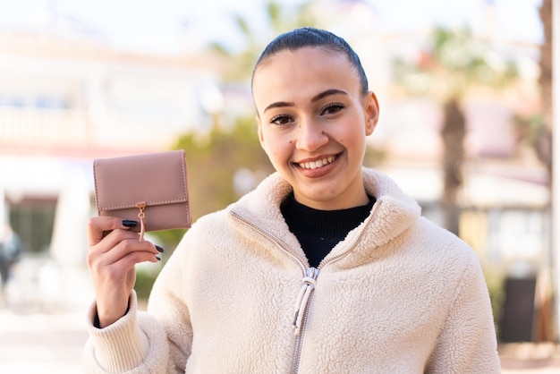 Jeune fille marocaine tenant un portefeuille à l'extérieur en souriant beaucoup