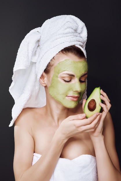 Jeune fille avec un masque cosmétique d'avocat. fond sombre, lumière de studio.