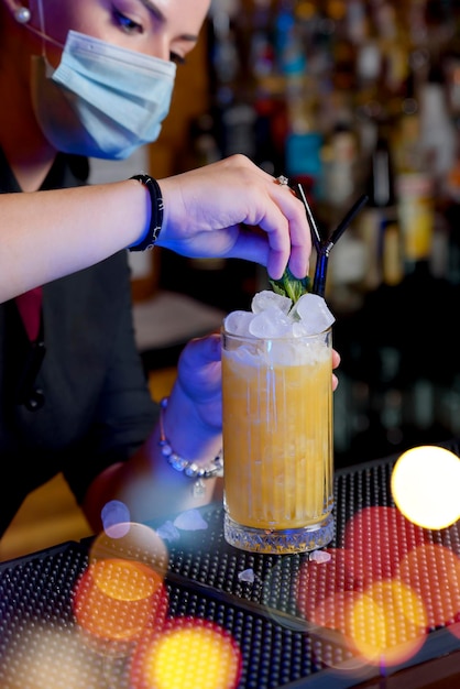 Jeune fille avec masque préparant un cocktail dans un verre de cristal. concept de barman