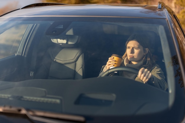 Jeune fille le matin va travailler en voiture et boire du café Vue à travers le pare-brise