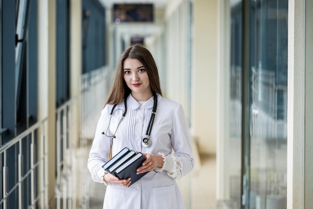 Une jeune fille médecin en blouse blanche avec un livre bleu dans les mains dans le couloir de l'hôpital