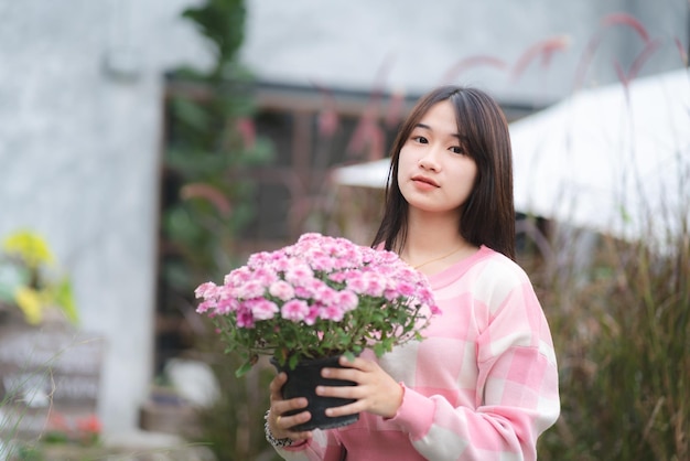 Jeune fille mignonne asiatique portant une chemise rose et tenant un modèle féminin de portrait de belle fleur rose avec le concept de la nature avec une fleur rose à la main heureuse et sourire à l'extérieur