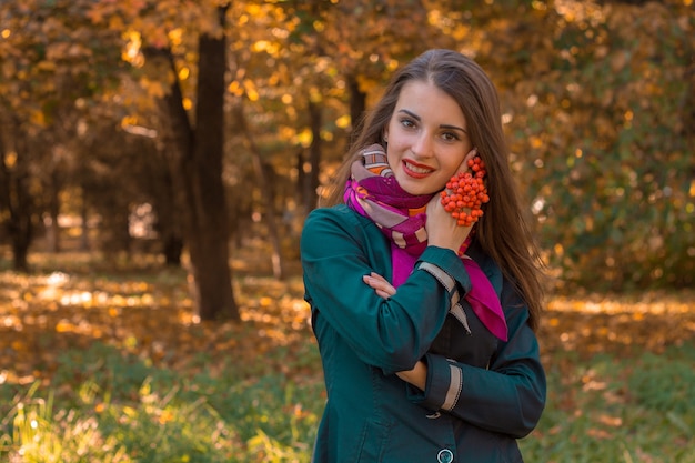 La jeune fille mignonne se tient en parc d'automne avec un brin de Rowan dans sa main