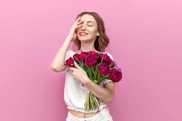 Une jeune fille mignonne en vêtements de fête tient un bouquet de fleurs et sourit sur un fond rose