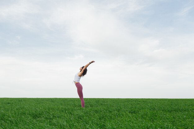 Jeune fille mince faisant du yoga en plein air dans un champ vert