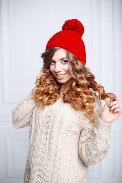 Jeune fille à la mode aux cheveux bouclés dans un bonnet rouge et pull vintage.