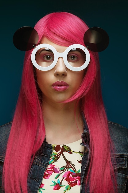 Jeune fille de mode aux cheveux roses et grandes lunettes de soleil sur fond bleu