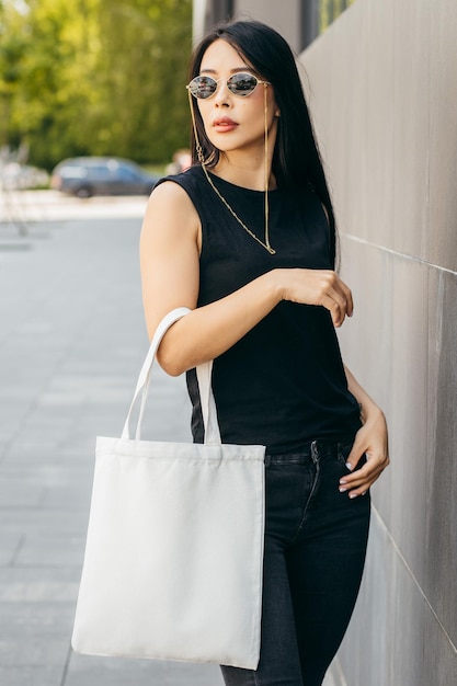 Jeune fille modèle asiatique dans la rue tenant une maquette de sac écologique blanc