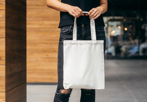 Jeune fille modèle asiatique vêtue d'un t-shirt blanc dans la rue tenant une maquette de sac écologique blanc