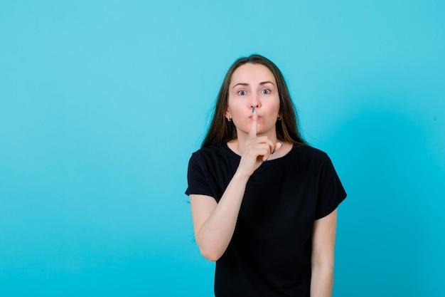 Jeune fille montre un geste de silence en mettant l'index sur les lèvres sur fond bleu