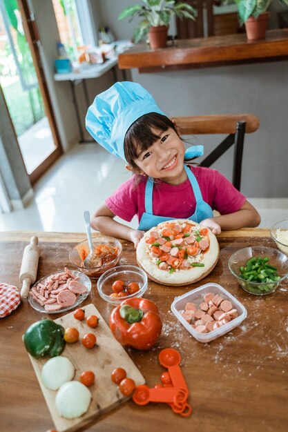 Jeune fille montre une pizza sur la table dans la cuisine