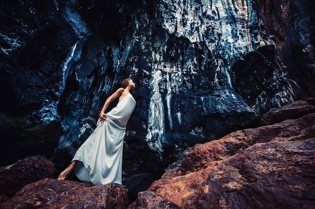 Une Jeune Fille Mystérieuse Dans Une Longue Robe Blanche - Un Modèle Caucasien Se Promène Parmi Les Roches Noires. Thème De Session Photo Gothique De Halloween. Tenue Inhabituelle Et Créative