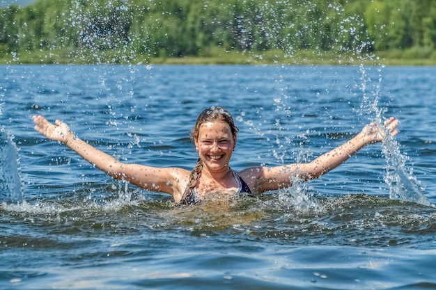 Une jeune fille nage et patauge dans le lac Des éclaboussures d'eau volent dans toutes les directions